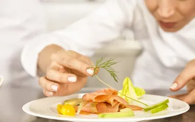 Salmon on a plate with a chef adding decorative greenery