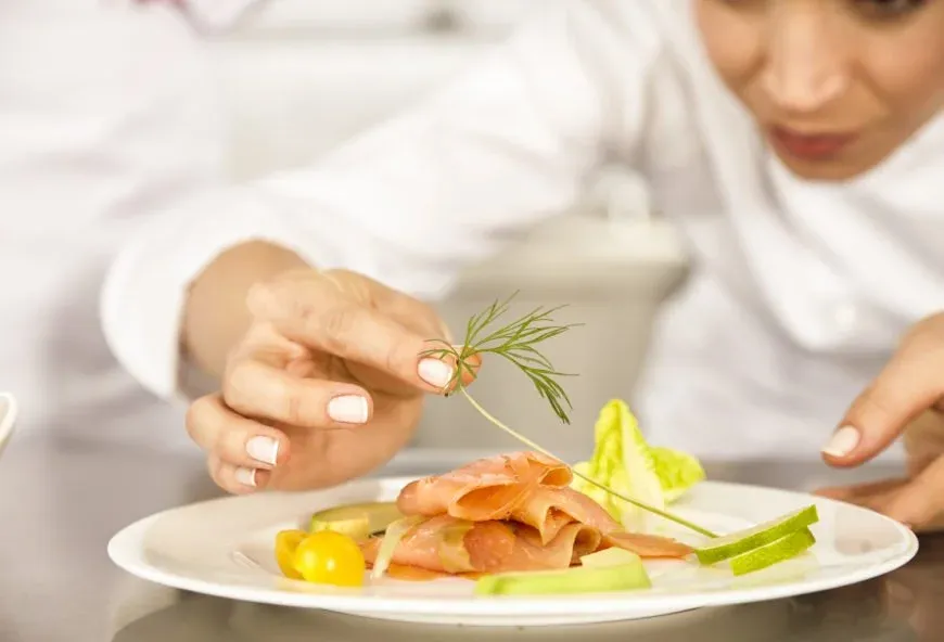 Salmon on a plate with a chef adding decorative greenery