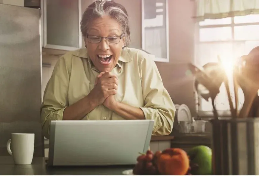 Woman looking very happy at a laptop in her kitchen