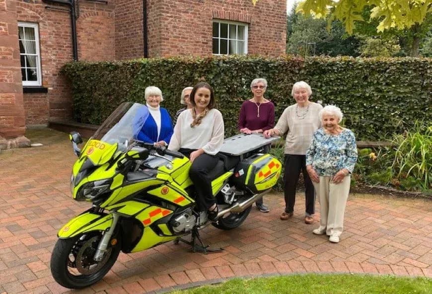 Cheshire Blood Bikes staff on a motorbike with Boughton Hall residents