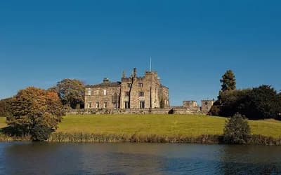Large stone House on a hill with a lake in front of it.