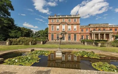 Hall in the sunshine with a pond in front of it.
