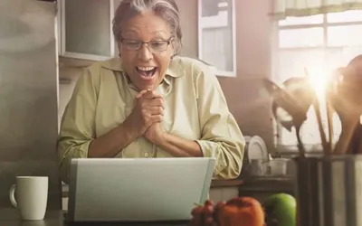 Woman looking very happy at a laptop in her kitchen