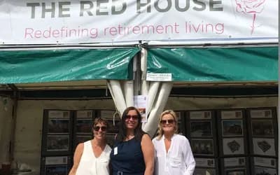 Three women with sunglasses on stood in front of a sign.