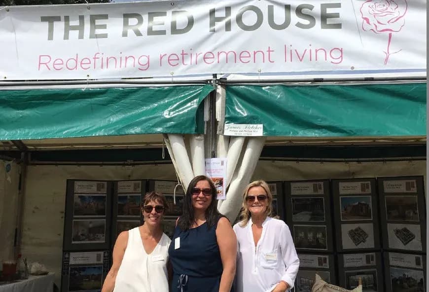 Three women with sunglasses on stood in front of a sign.