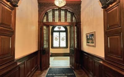 Ornate entrance hallway at St Mary’s Convent School in Worcester featuring carved wood paneling, stained glass windows and chandelier lighting.