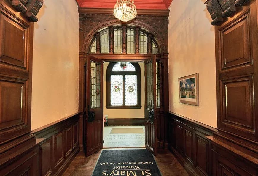 Ornate entrance hallway at St Mary’s Convent School in Worcester featuring carved wood paneling, stained glass windows and chandelier lighting.